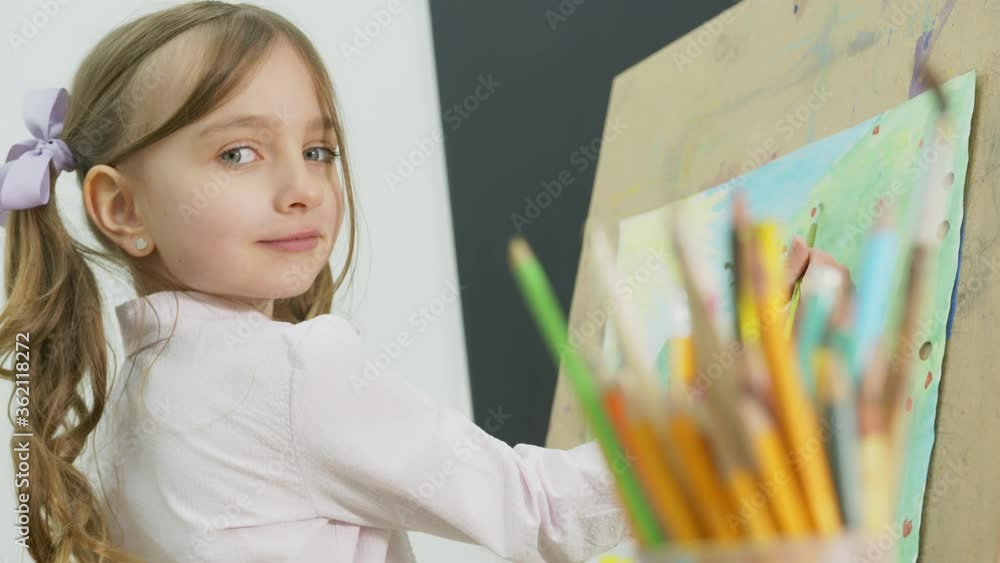 little girl paints a picture and looks at the camera. Happy little girl ...