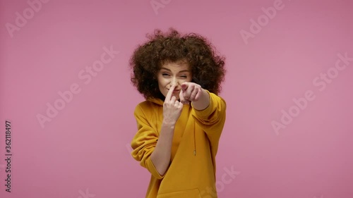 You tell lie! Girl afro hairstyle in hoodie looking with suspicion, touching nose showing liar gesture and pointing to camera, distrust falsehood concept. studio shot isolated on pink background