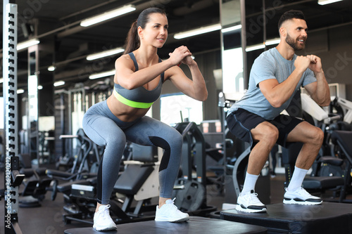 Fit couple doing jumping squats in crossfit gym.
