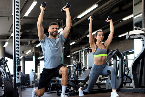 Attractive sports people are working out with dumbbells at gym.