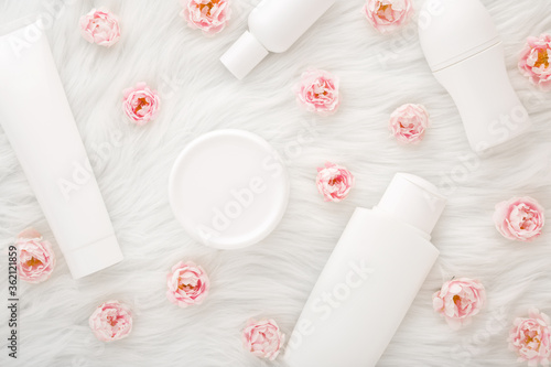 Different white toiletries and pink roses on fluffy fur blanket background. Care about face, hands, legs and body skin. Daily women beauty products. Flat lay. Closeup. Top down view.