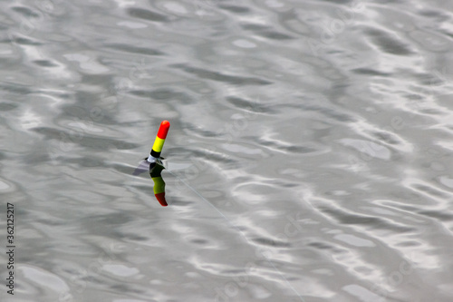 Fishing float (bobber) against the background of water close-up. small waves and reflections of the sun on the surface of the water. fishing concept and place for text.