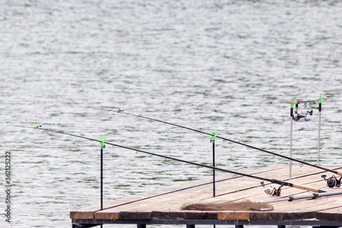 Professional fishing rods are lying on a wooden pier hanging over the water. concept for the day of the fisherman. Outdoor recreation in summer and autumn.
