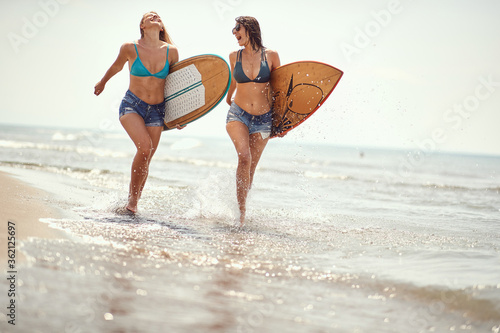 female surfers running on the beach holding surfboards, laughing