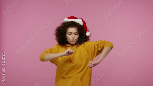 Funny positive girl afro hairstyle with Santa Claus hat dancing and singing, feeling carefree happy, moving in energetic dance, relaxing on Christmas party. studio shot isolated on pink background