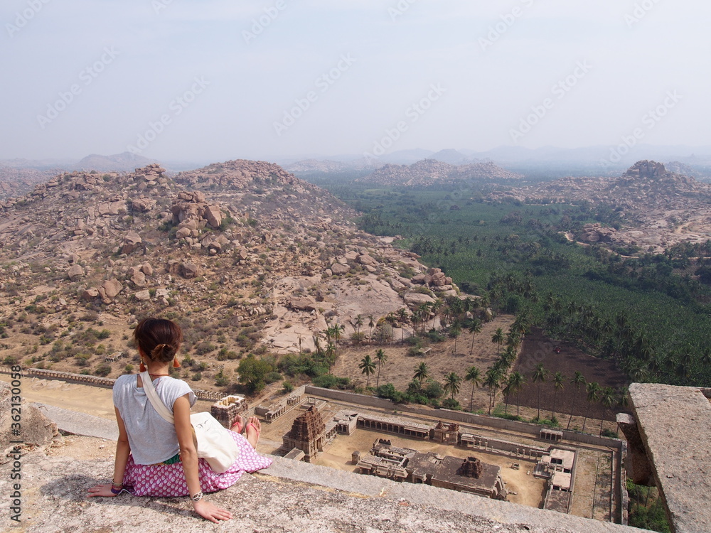 A woman is sitting in a vantage point, looking at the ruins, Hampi, Karnataka, South India, India