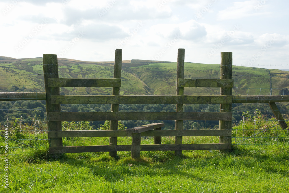 Wooden stile across a fence, leading from a cliff edge to the valley beyond.