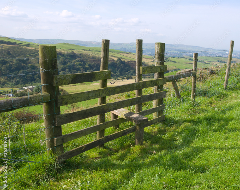 Wooden stile across a fence, leading from a cliff edge to the valley beyond.