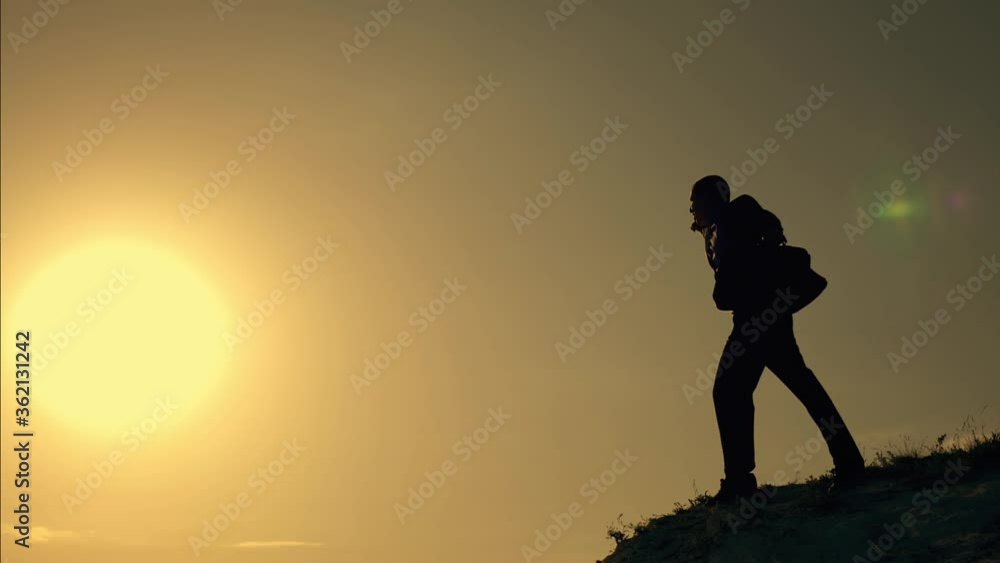 A businessman in a suit on top of a mountain. A successful person seeks victory, to achieve a goal, success. The concept of teamwork. Silhouette of man pulling emotionally hand up, symbol of victory. A businessman in a suit on top of a mountain. A successful person seeks victory, to achieve a goal, success. The concept of teamwork. Silhouette of man pulling emotionally hand up, symbol of victory.