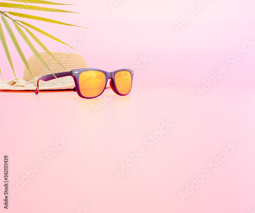 summer accessories concept from sunglasses, straw hat and palm leaf on pastel pink background. web banner size.