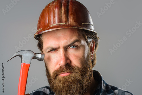 Worker holds hammer. Builder with hammer. Portrait of bearded workman. Building, industry, technology. Builder in hard hat. Advertise. Repairment. Mechanical worker.