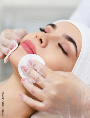 Close up of beautician hands doing facial cleansing of a young woman using cotton pads or sponge in a beauty clinic or spa. Cosmetology treatment. Perfect skin concept. Eternal youth.
