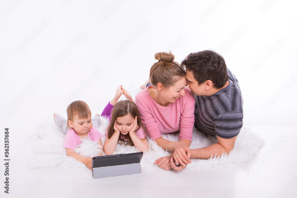 the kids are watching cartoons on the tablet. a man and a woman embrace. Family vacation, joint pastime. Parents with girls on the floor the kids are watching cartoons on the tablet. a man and a woman embrace. Family vacation, joint pastime. Parents with girls on the floor