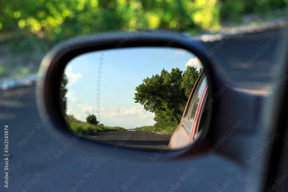 trees and highway in car rearview mirror