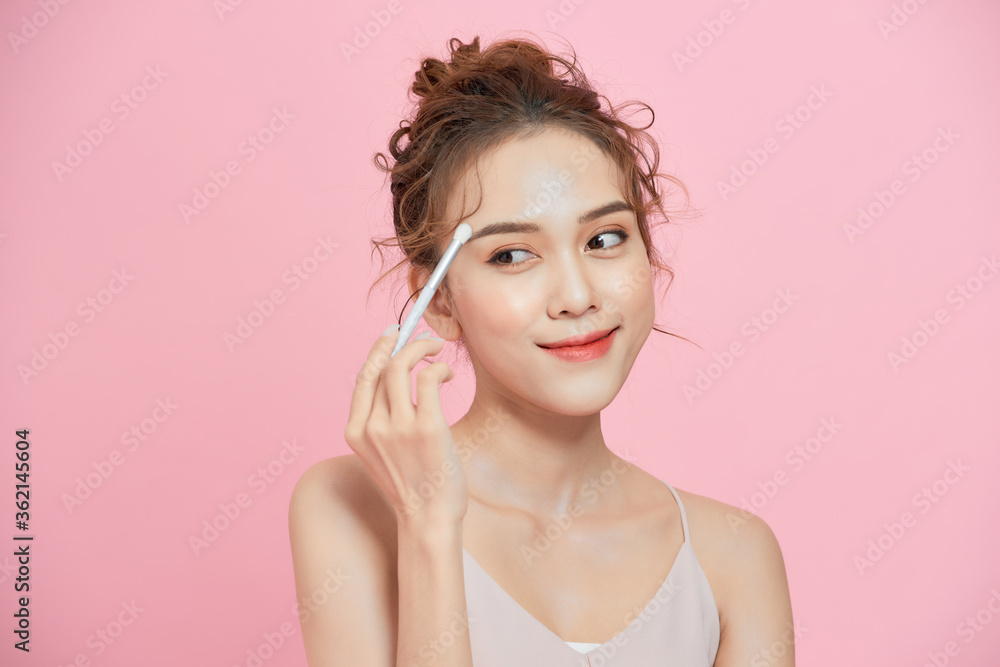 Portrait of excited young Asian woman holding brush and applying makeup over pink background. Portrait of excited young Asian woman holding brush and applying makeup over pink background.