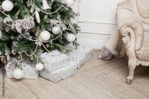 Christmas tree with silver toys on a derelict floor in the interior. Gifts in gift wrapping. New Year celebration. Space for text. Close-up. Blurred.