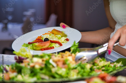 Selective focus on a plate full of salad in the hand of a woman picking up food from a buffet