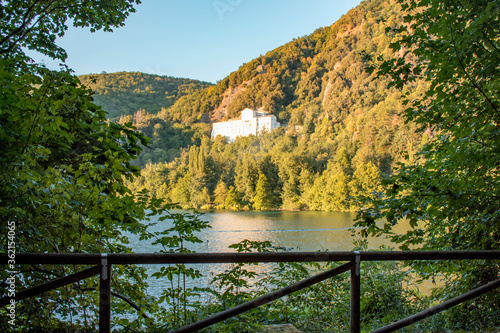 skyline of Monticchio lake in the sunset. It is an amazing lake with church near them. The lake is in a wonderful forest with a lot of trees on the hills with a white church photo