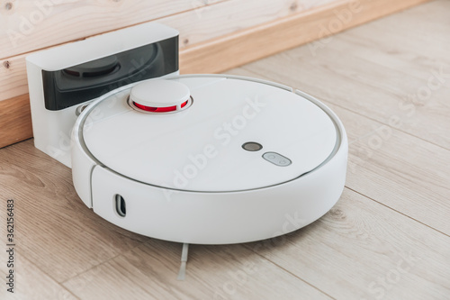 Wireless robot vacuum cleaner return to charging at dock in clean wooden floor.