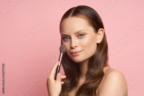 Beauty makeup. Young girl with makeup brush in hands on pink background
