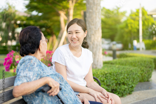 Grandma sitting beside her granddaughter in a park. Young woman taking care of elder person in a family. Wellness, wellbeing and healthcare concept.