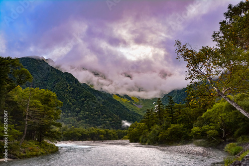Foto 北アルプスの梓川と深緑の森、上高地から見上げた岳沢カール、虹色の雲に覆われる穂高連峰、（西穂高岳、赤岩岳、間ノ岳、天狗岩、天狗のコル、ジャンダルム、ロバの耳、奥穂高岳、吊尾根、前穂高岳、明神岳）。観光名所。景勝地。中部山岳国立公園。上流。Hodaka mountain range looking up from Kamikochi
