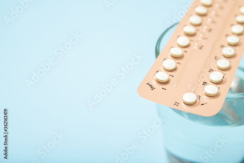 Female oral contraceptives and a glass of water on a blue background. Close-up, place for text.