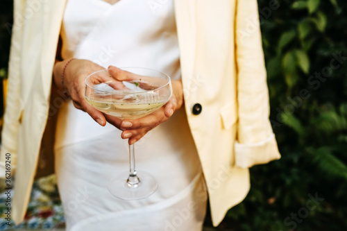 Woman dressed in white cocktail dress holding a coupe of champagne. photo