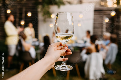 Canvas Print Female hand holding a glass of white wine on a blurred table background, outdoors
