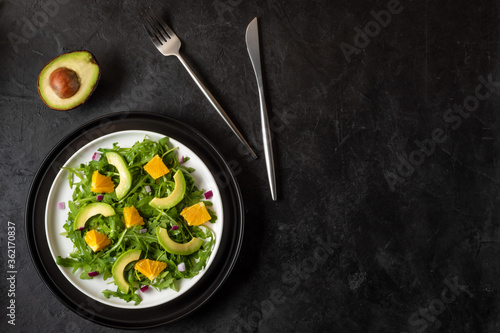 Salad with avocado, orange, ruccola and red onion on black stone background. Horizontal orientation. Flat lay. Copy space.