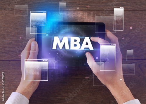 Close-up of a hand holding tablet with MBA abbreviation, modern technology concept
