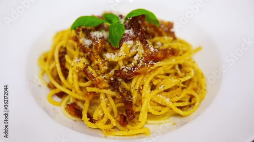 Pasta Carbonara. Spaghetti with bacon, parmesan cheese, and basil leaf. Pasta Carbonara on a white plate with parmesan on a dark background. Italian food concept. Close up.