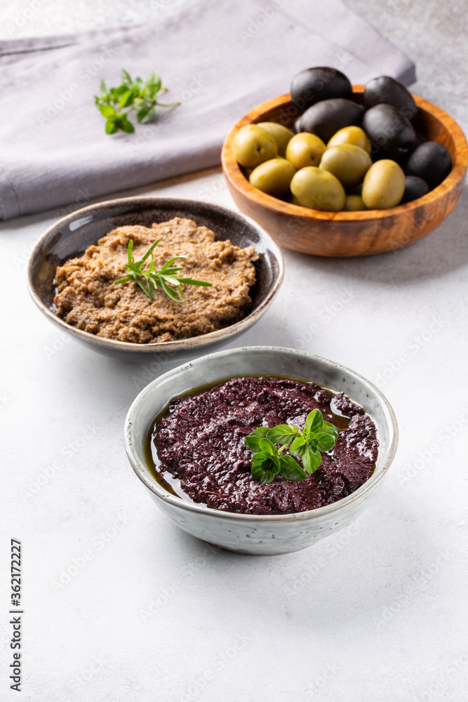 Tapenade - paste made from olives. Bowls with spreadable black and green olive cream on concrete background. Tapenade - paste made from olives. Bowls with spreadable black and green olive cream on concrete background.