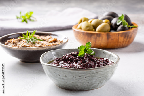 Tapenade - paste made from olives. Bowls with spreadable black and green olive cream on concrete background. photo