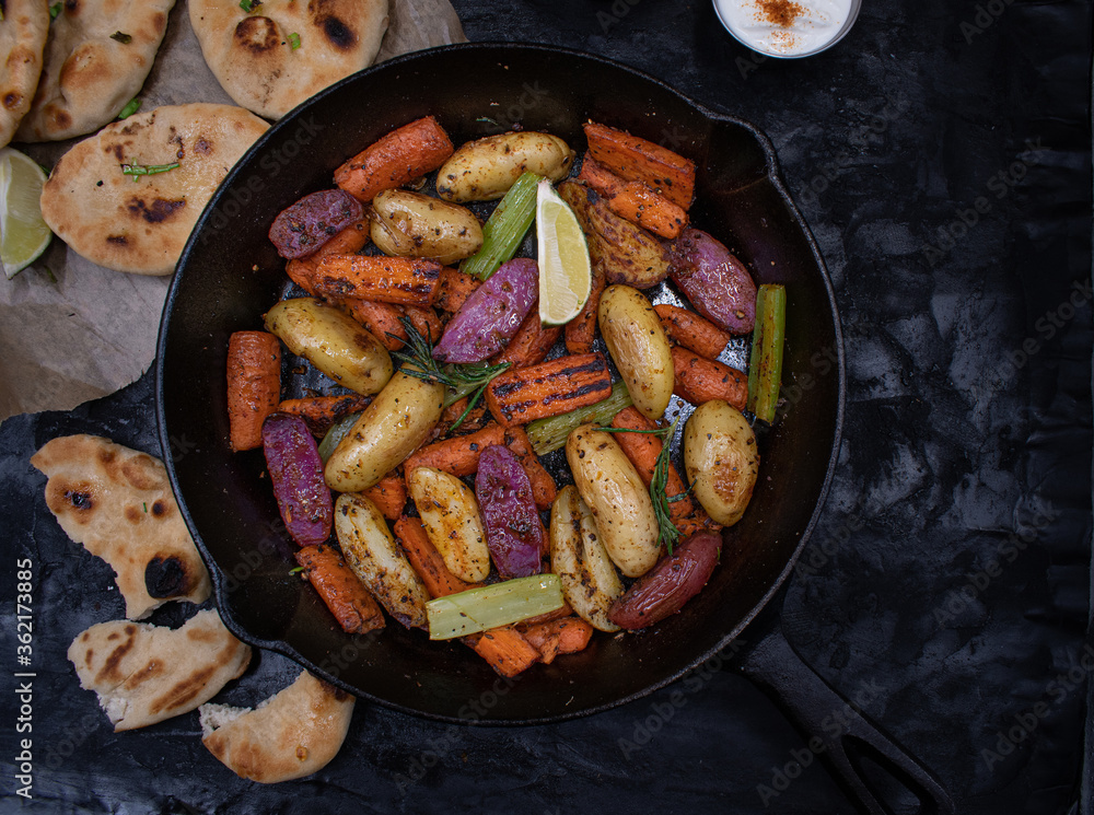 Roasted potatoes and carrots, celery and herbs in cast iron pan on dark table, copy space Roasted potatoes and carrots, celery and herbs in cast iron pan on dark table, copy space