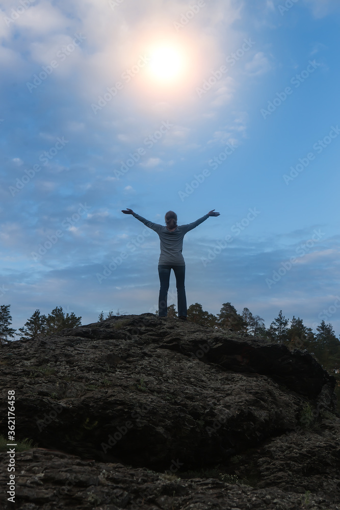 Woman on top of the mountain stretches her arms to the sun