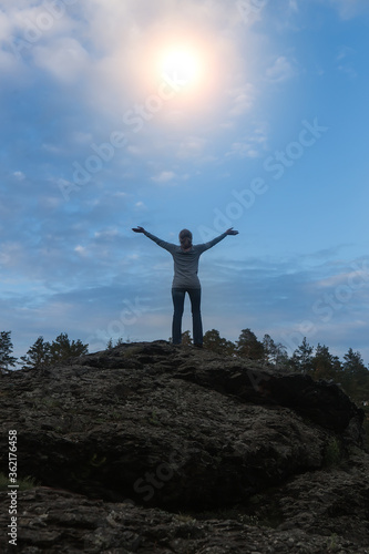 Woman on top of the mountain stretches her arms to the sun