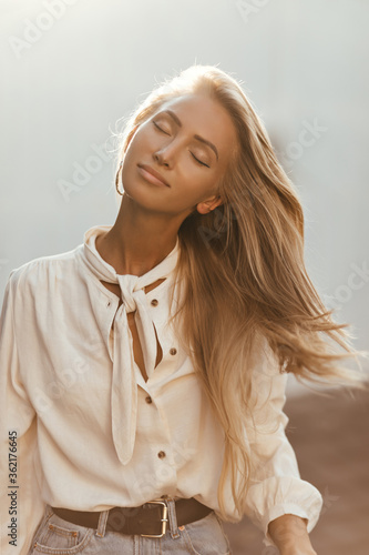 Tableau sur toile Happy blonde woman in white blouse and denim skirt plays hair