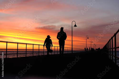 Silhouettes of two people walking on the jetty at civil twilight time.