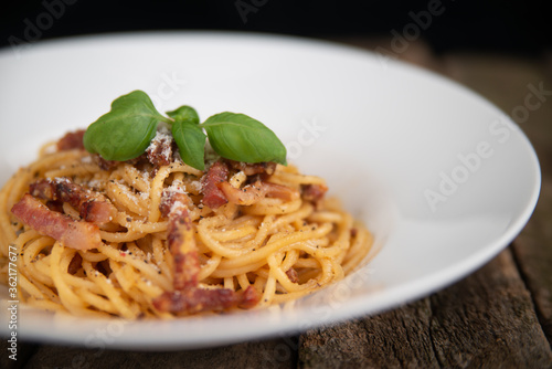 Pasta Carbonara. Spaghetti with bacon, parmesan cheese, and basil leaf. Pasta Carbonara on a white plate with parmesan on a dark background. Italian food concept. Close up.