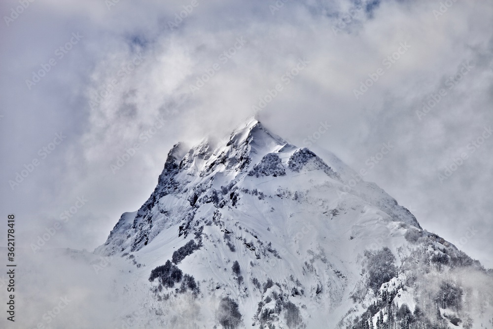 Snowcapped mountain peak among the clouds. Snowy mountains winter landscape on cloudy sky background. Winter snowy day in mountains. Snow-covered white mountain top. Snowy mountain range.