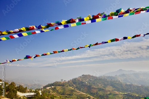 Bright colorful Prayer flags on Himalaya mountains landscape and clear blue sky background. Hiking in Himalaya mountains. Beautiful panoramic Himalaya mountains landscape view. Flags in the sky. 