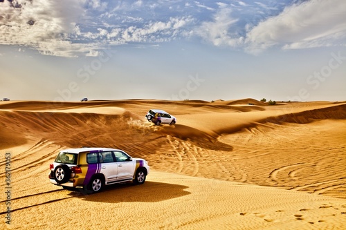 Off road cars riding fast on dunes slopes in the desert in hot sunny day. Car safari among sand dunes in the desert. Traveling by car in the desert. 4x4 cars. Off road trip. Desert off-road racing. © ST-art
