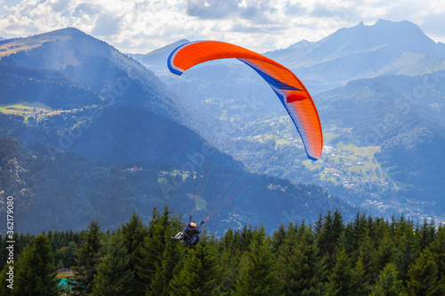 Paragliding high among the mountains in sunny summer day. Extreme Sports in the Mountains. Paraglider flight on mountains and bright sunny sky background. People Flying high in the sky. Freedom