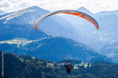 Paragliding flight high among the mountains in sunny summer day. Extreme Sports in the Mountains. Paraglider flight on mountains and bright sunny sky background. People Flying high in the sky. Freedom