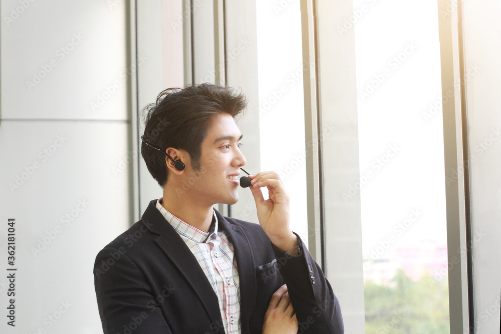 Smiling handsome Businessman Call Center standing near glass wall. Technical Support staff. Asian customer support team. Smiling handsome Businessman Call Center standing near glass wall. Technical Support staff. Asian customer support team.