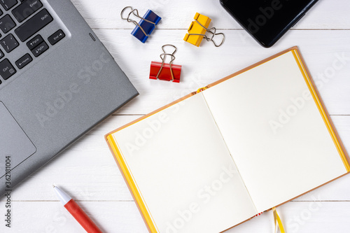 Laptop cellphone paper clips and notepad on white wooden background