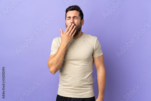 Young handsome man with beard over isolated background yawning and covering wide open mouth with hand