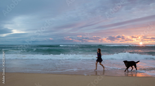 cute little girl running on the beach with her dog at sunset
