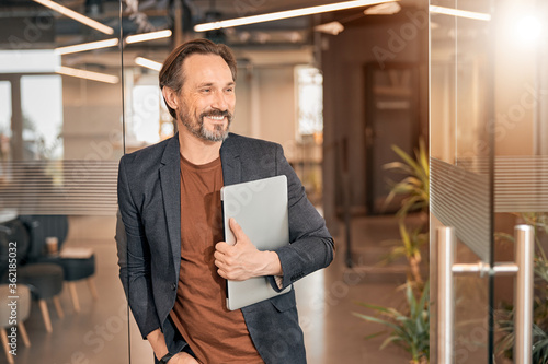 Bearded businessman holding laptop standing in modern office